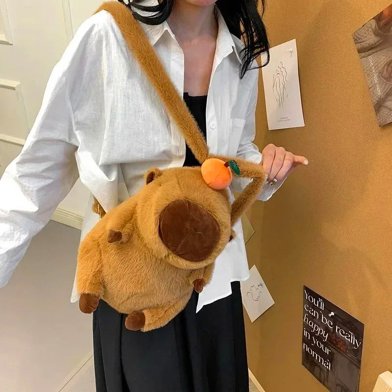 Capybara backpack with orange fruit hat worn crossbody by woman in white shirt