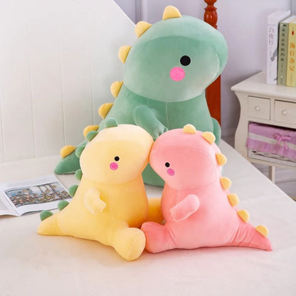 Octoplush Kawaii collection of soft and squishable dinosaur plushies in pastel green, yellow, and pink. This adorable dino trio from Octoplush.store is shown in small and large sizes on a bed, featuring cute rosy cheeks and yellow spikes, perfect for aesthetic room decor and matching best friend gifts.