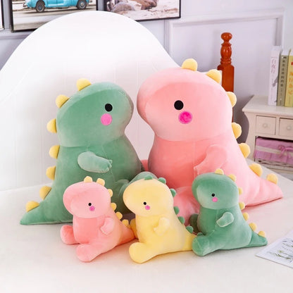 The Octoplush Kawaii collection featuring a family of soft and squishable dinosaur plushies in pastel pink, green, and yellow. This assortment of cute dino stuffed animals includes various sizes from small to large, all with signature yellow spikes and rosy cheeks, perfect for aesthetic bedroom decor and gifts.