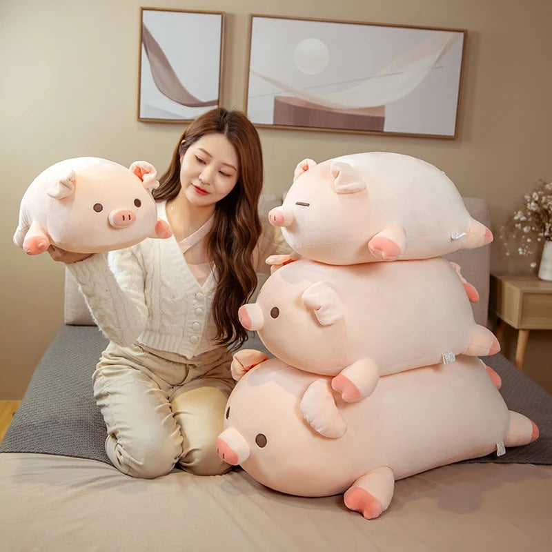 A full collection of pink kawaii squishy piggy plushies in small, medium, and large sizes stacked on a bed to show the complete set.