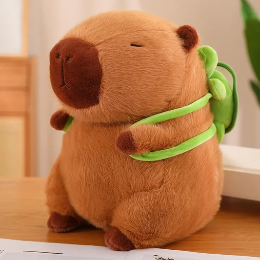 Side view of a soft capybara stuffed animal sitting upright on a table, showcasing its chubby shape and green turtle backpack detail.